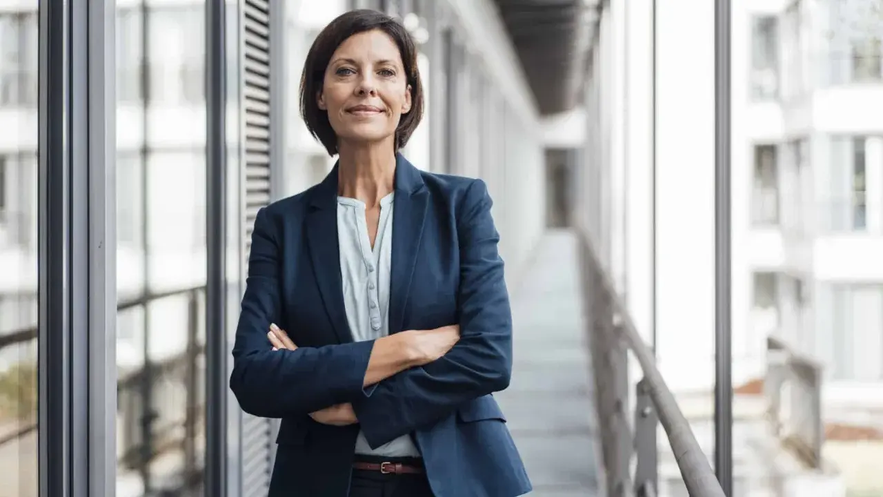 Donna in giacca blu con braccia conserte, sorride. Potrebbe essere un'area manager che discute del suo stipendio.