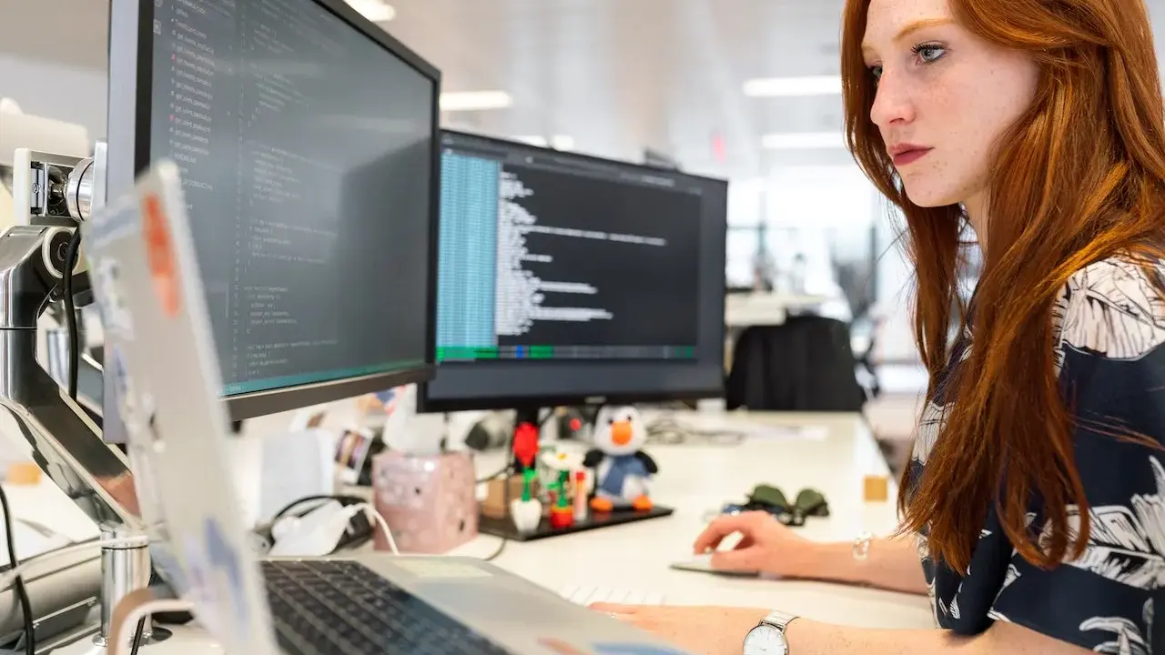 Donna con capelli rossi lavora al computer, analizzando codice. Un ingegnere gestionale cosa fa? Ottimizza processi e sistemi, proprio come lei con i dati.