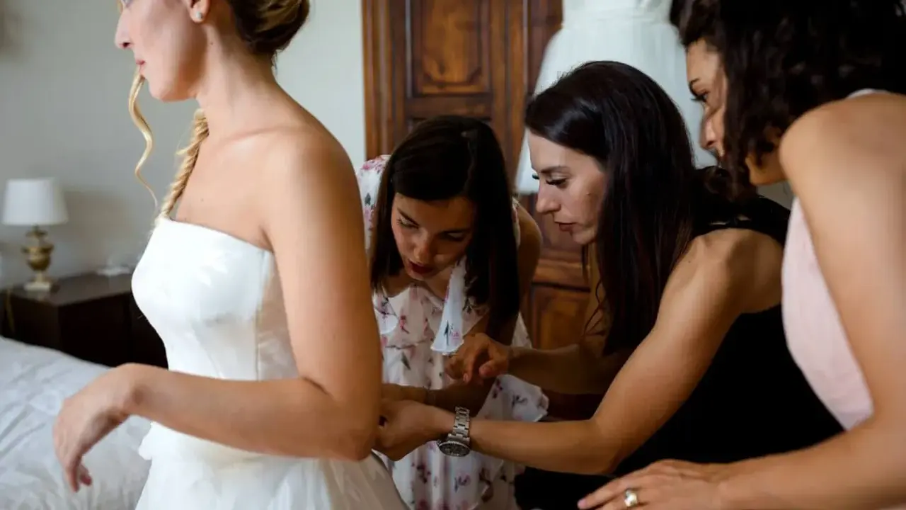 Sposa in abito bianco, aiutata da amiche e forse da una wedding planner, si prepara per il grande giorno.