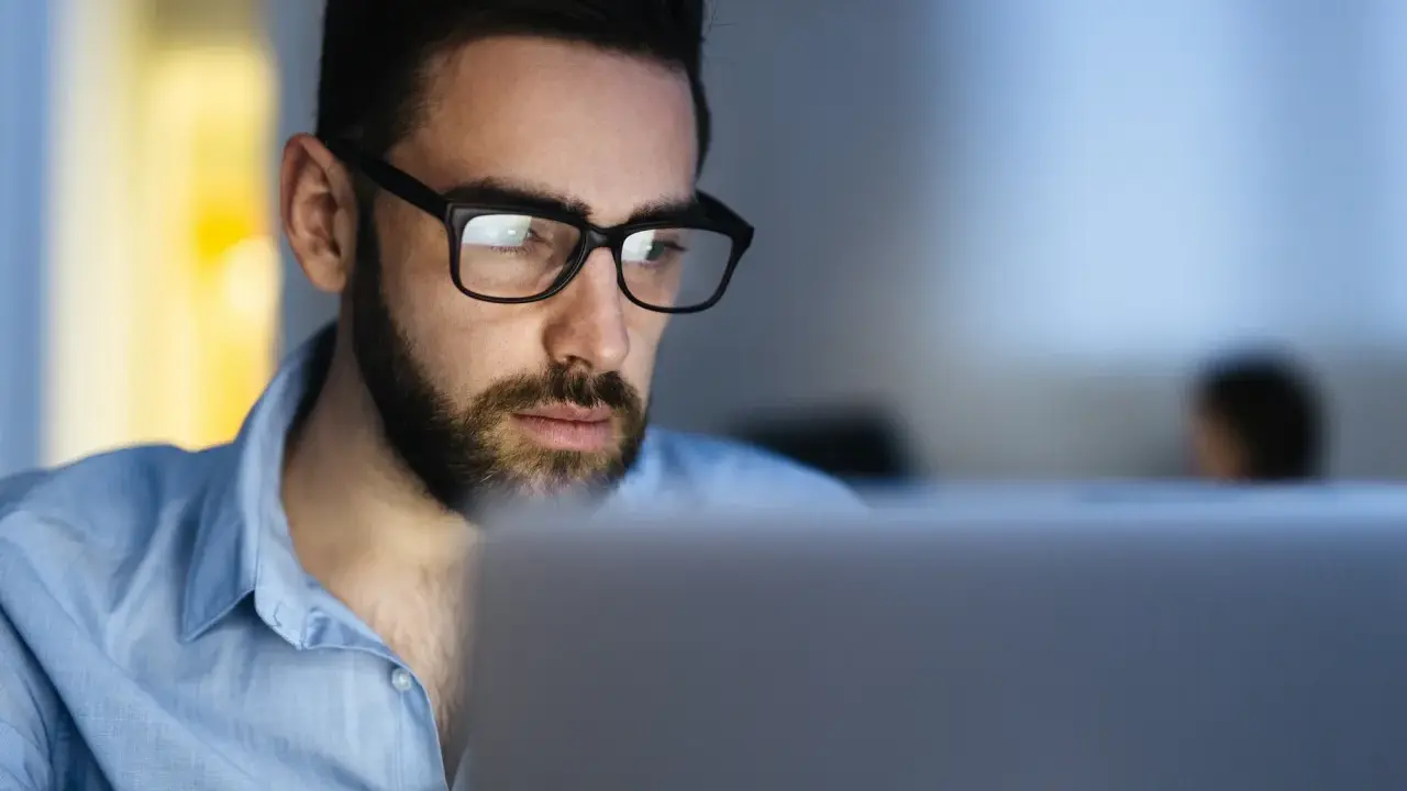 Uomo con occhiali studia al computer, concentrato su un corso di paghe e contributi.
