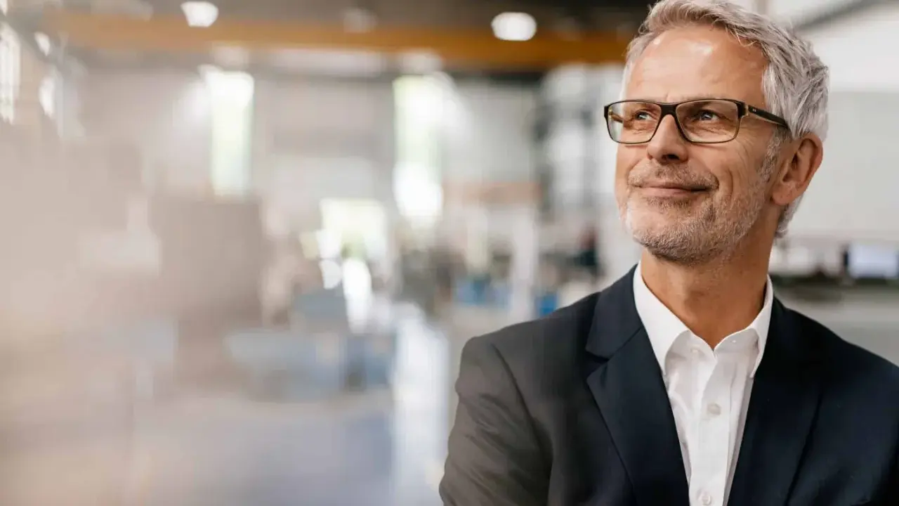 Uomo d'affari con occhiali, sorride guardando in alto, pensando ai suoi prossimi corsi export manager.