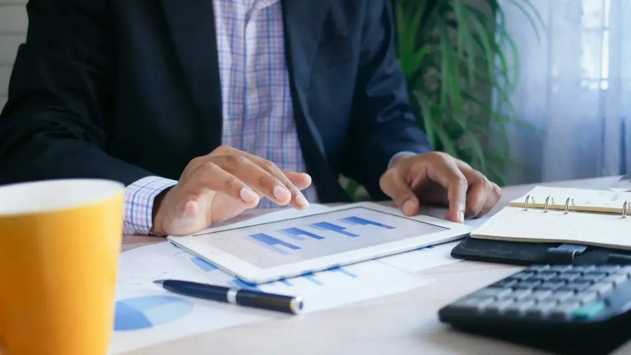 Uomo d'affari analizza grafici su tablet, con tazza, calcolatrice e agenda. Un esempio di come trovare lavoro a 60 anni con nuove competenze.