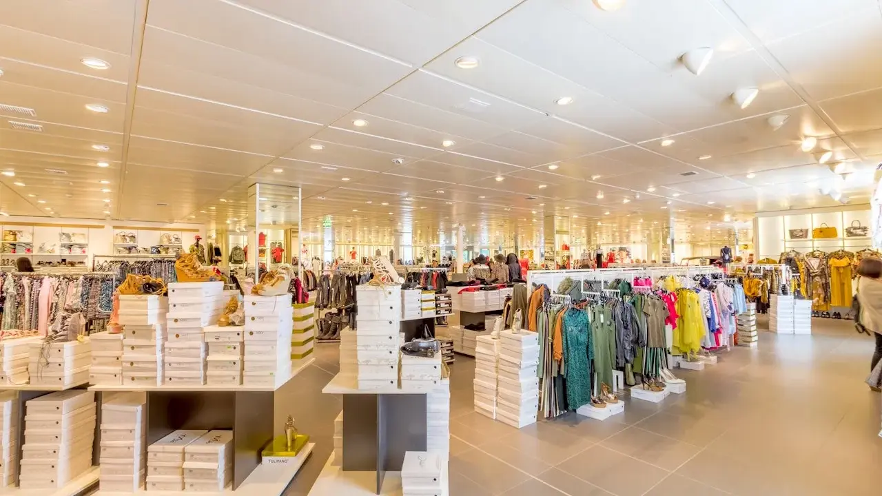 Interno di un negozio di abbigliamento con scaffali pieni di scarpe e vestiti. Un banconista cosa fa? Probabilmente sistema la merce per renderla accattivante.