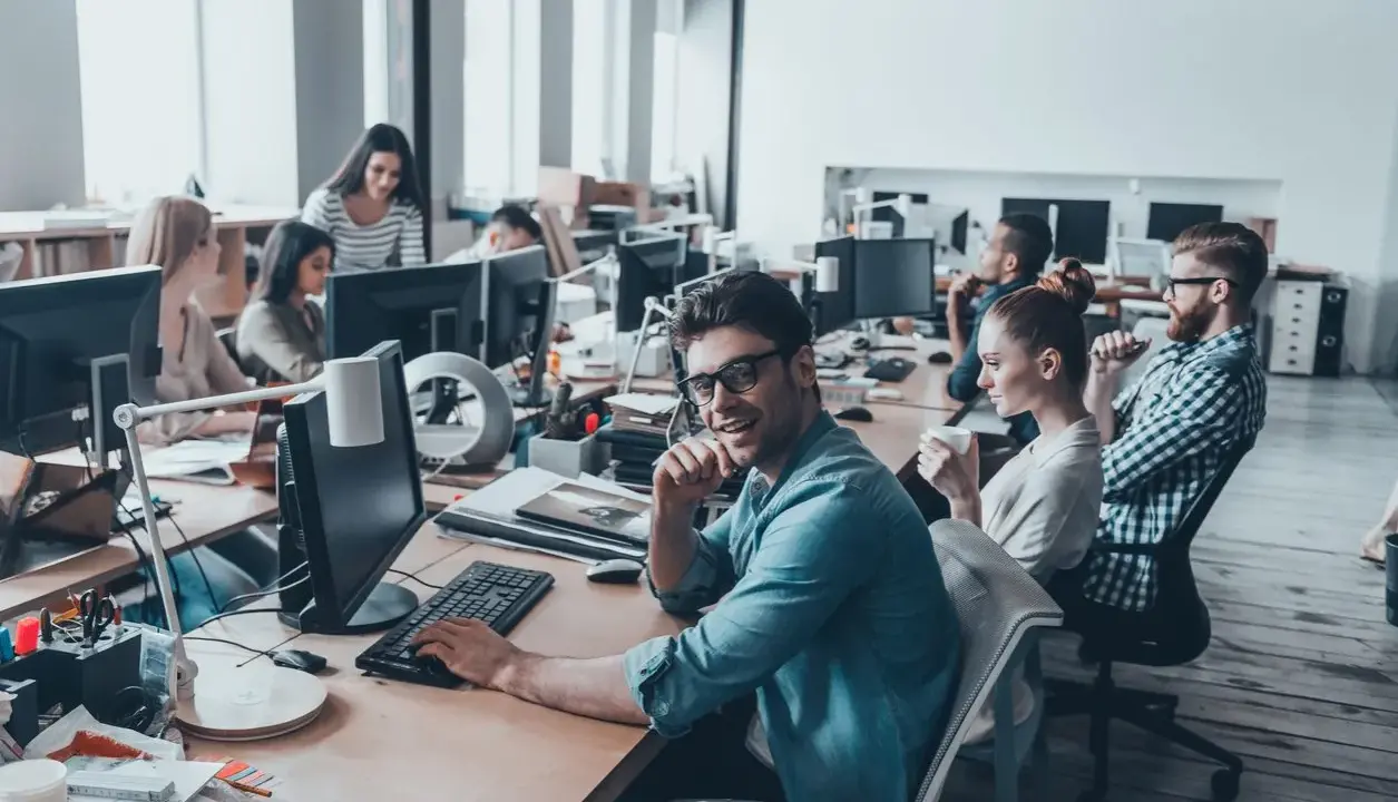 Ufficio moderno con persone al lavoro. Si discute di ccnl grafici editoriali livelli e mansioni, tra scrivanie e computer.