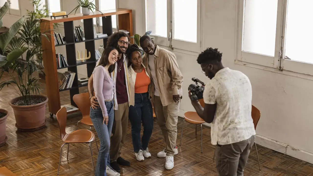 Gruppo di amici sorridenti durante un corso ufficio stampa, uno di loro scatta una foto con il cellulare.