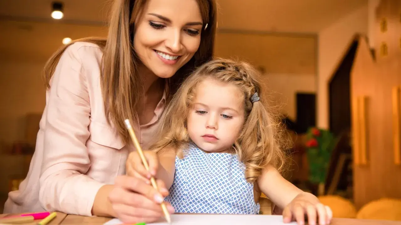 Un educatore professionale guida una bambina nel disegno, con matite colorate sparse sul tavolo.