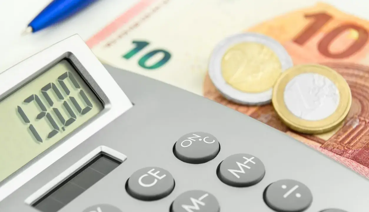Calcolatrice con display "13.00", banconote da 10 euro e monete. Un promemoria visivo di quando viene pagata la 13esima.