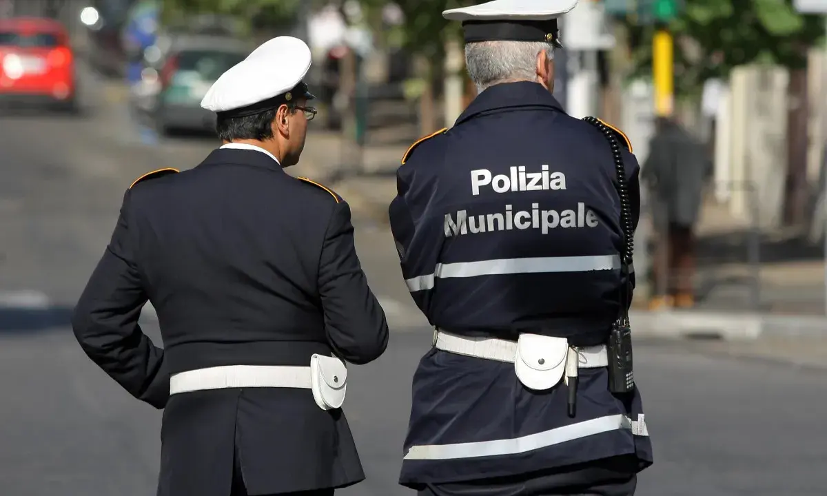 Due vigili urbani in divisa, uno con la scritta "Polizia Municipale" sulla schiena, in attesa di un equo stipendio.