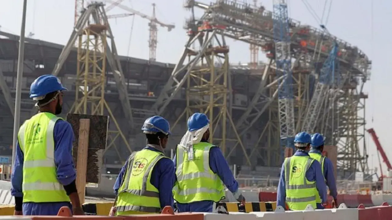 Operai con caschi e giubbotti ad alta visibilità lavorano in Qatar alla costruzione di un imponente stadio.