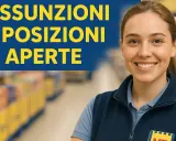Giovane scaffalista supermercato sorridente, con scritta "Assunzioni e posizioni aperte".