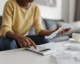 Donna calcola il suo stipendio part time con una calcolatrice, circondata da bollette e documenti.
