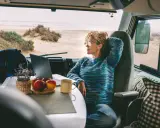 Donna con capelli ricci lavora al computer in un camper, godendosi la vista del mare. Un esempio di nomade digitale lavoro.