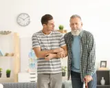 Giovane uomo supporta un anziano con bastone, entrambi con espressione speranzosa per un'aspettativa lavoro tempo indeterminato.