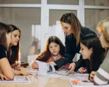 Una pedagogista guida un gruppo di ragazze nello studio, mostrando loro come affrontare un libro.