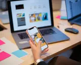 Un ux designer valuta un'interfaccia utente su smartphone, con laptop e post-it colorati sulla scrivania.
