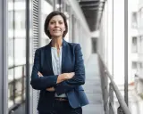 Donna in giacca blu con braccia conserte, sorride. Potrebbe essere un'area manager che discute del suo stipendio.