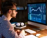 Uomo con occhiali analizza grafici finanziari al computer, comprendendo il broker significato.