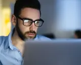 Uomo con occhiali studia al computer, concentrato su un corso di paghe e contributi.