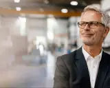 Uomo d'affari con occhiali, sorride guardando in alto, pensando ai suoi prossimi corsi export manager.