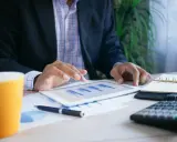 Uomo d'affari analizza grafici su tablet, con tazza, calcolatrice e agenda. Un esempio di come trovare lavoro a 60 anni con nuove competenze.