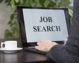 Persona che digita su un laptop con scritto "JOB SEARCH". Un caffè è accanto, pronto per iniziare a cercare lavoro.