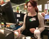 Cassiera al supermercato, Allie, con il suo nome visibile, lavora al registratore di cassa. Il suo stipendio da cassiera di supermercato è guadagnato con ogni transazione.