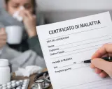 Medico compila certificato di malattia per un lavoratore. Sul tavolo, farmaci e stetoscopio, mentre sullo sfondo una persona malata beve una tisana.