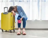 Donna esausta con valigia gialla e passaporto, vorrebbe essere in ferie ma è in malattia.