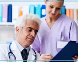 Medico anziano e giovane assistente studiano insieme un referto. Un'immagine che evoca il **corso assistente studio medico**.