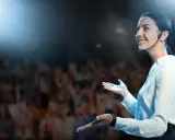 Oratrice sorridente sul palco, con microfono, che parla a un pubblico. Nonostante l'ansia, non riesco a parlare in modo fluido, ma cerco di comunicare.