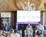 Panel di esperti discute di architetture digitali. Uno dei relatori, con un completo blu, sembra pensare: "non so che lavoro fare".