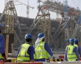 Operai con caschi e giubbotti ad alta visibilità lavorano in Qatar alla costruzione di un imponente stadio.