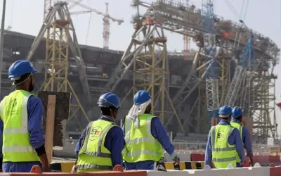 Operai con caschi e giubbotti ad alta visibilità lavorano in Qatar alla costruzione di un imponente stadio.
