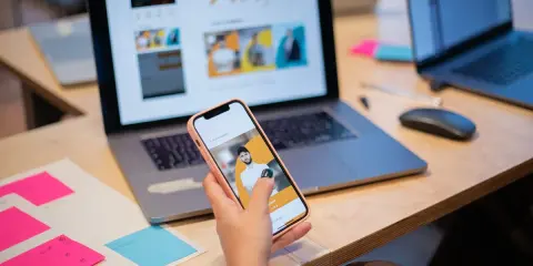 Un ux designer valuta un'interfaccia utente su smartphone, con laptop e post-it colorati sulla scrivania.