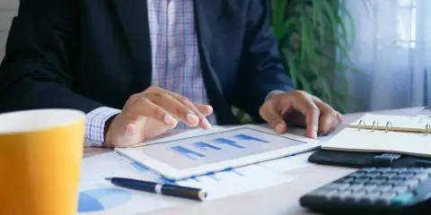 Uomo d'affari analizza grafici su tablet, con tazza, calcolatrice e agenda. Un esempio di come trovare lavoro a 60 anni con nuove competenze.