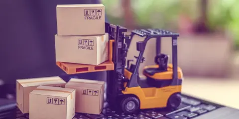 Carrellino elevatore giallo solleva scatole fragili su un pallet, mentre altre scatole attendono su una tastiera. Il buyer cosa fa? Organizza la spedizione.