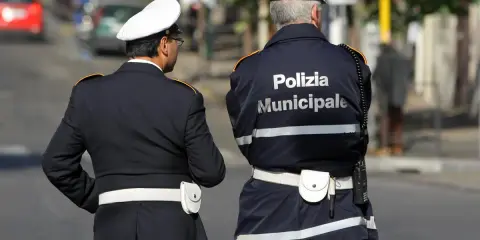 Due vigili urbani in divisa, uno con la scritta "Polizia Municipale" sulla schiena, in attesa di un equo stipendio.