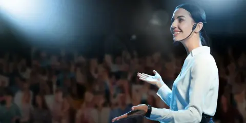 Oratrice sorridente sul palco, con microfono, che parla a un pubblico. Nonostante l'ansia, non riesco a parlare in modo fluido, ma cerco di comunicare.
