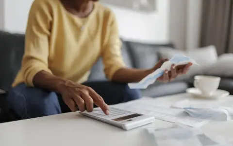 Donna calcola il suo stipendio part time con una calcolatrice, circondata da bollette e documenti.