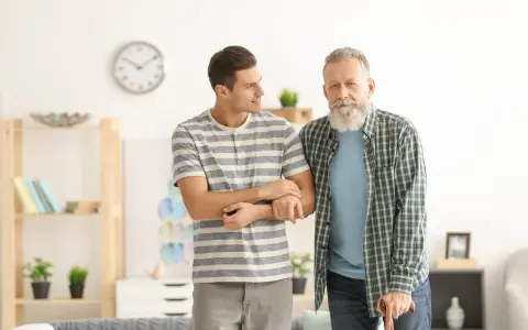 Giovane uomo supporta un anziano con bastone, entrambi con espressione speranzosa per un'aspettativa lavoro tempo indeterminato.