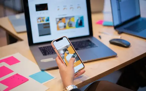 Un ux designer valuta un'interfaccia utente su smartphone, con laptop e post-it colorati sulla scrivania.