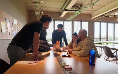 Un gruppo di giovani collabora attorno a un tavolo, un vero team di creator digitale che discute idee davanti a un laptop.