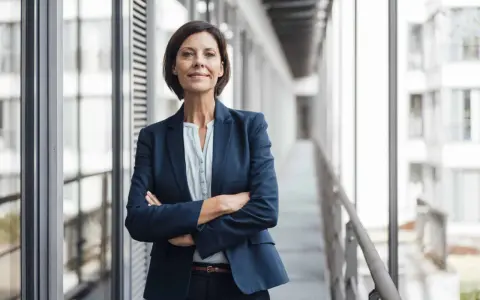Donna in giacca blu con braccia conserte, sorride. Potrebbe essere un'area manager che discute del suo stipendio.