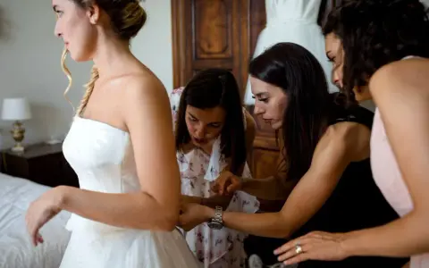 Sposa in abito bianco, aiutata da amiche e forse da una wedding planner, si prepara per il grande giorno.