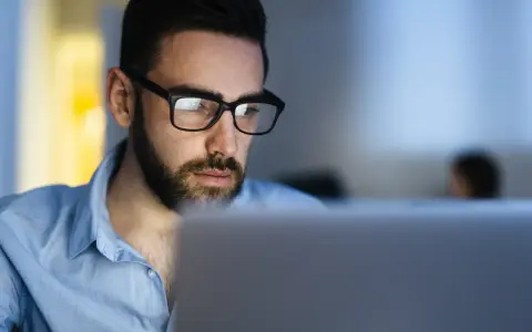 Uomo con occhiali studia al computer, concentrato su un corso di paghe e contributi.
