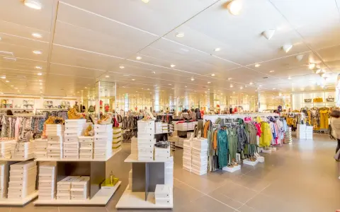 Interno di un negozio di abbigliamento con scaffali pieni di scarpe e vestiti. Un banconista cosa fa? Probabilmente sistema la merce per renderla accattivante.