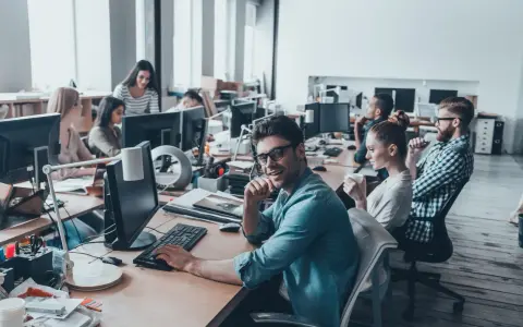Ufficio moderno con persone al lavoro. Si discute di ccnl grafici editoriali livelli e mansioni, tra scrivanie e computer.