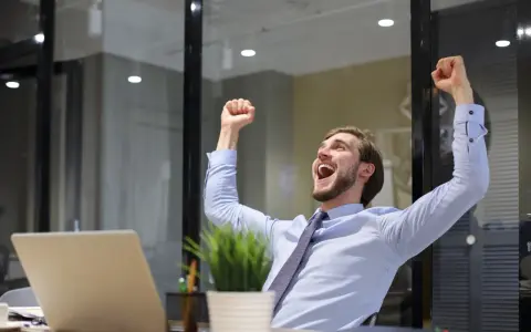 Uomo esulta alla scrivania, felice per un lavoro nella pubblica amministrazione senza concorso.