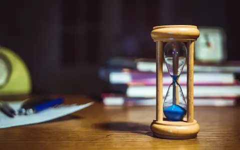 Clessidra con sabbia blu su una scrivania, a simboleggiare quante ore devono passare tra un turno e l'altro. Libri e fogli sullo sfondo.