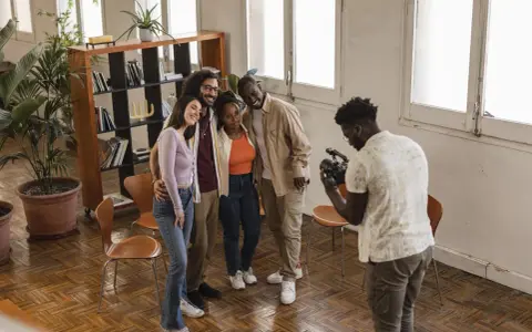 Gruppo di amici sorridenti durante un corso ufficio stampa, uno di loro scatta una foto con il cellulare.